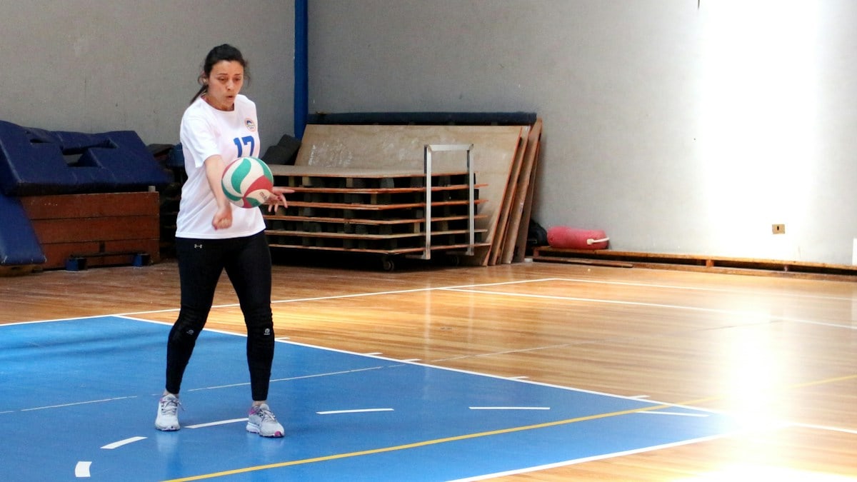 A woman in a white jersey bumping a volleyball on a wooden court